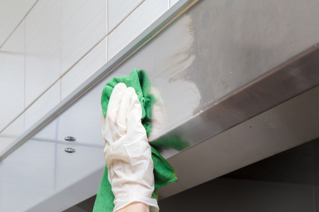 Hand cleaning the upper part of a wall with a green cloth